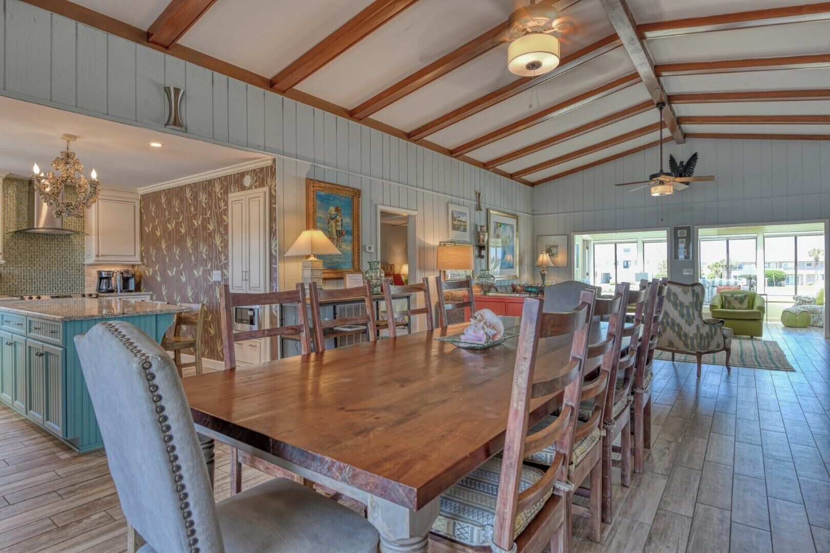 A spacious dining area with a wooden table and chairs, a kitchen with blue cabinets, and a large window providing natural light.
