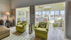 A spacious living room with a view of a pool and a balcony, furnished with green chairs and a lamp. - Pop's Place in the private gated community of Inlet Harbour (Garden City Beach)