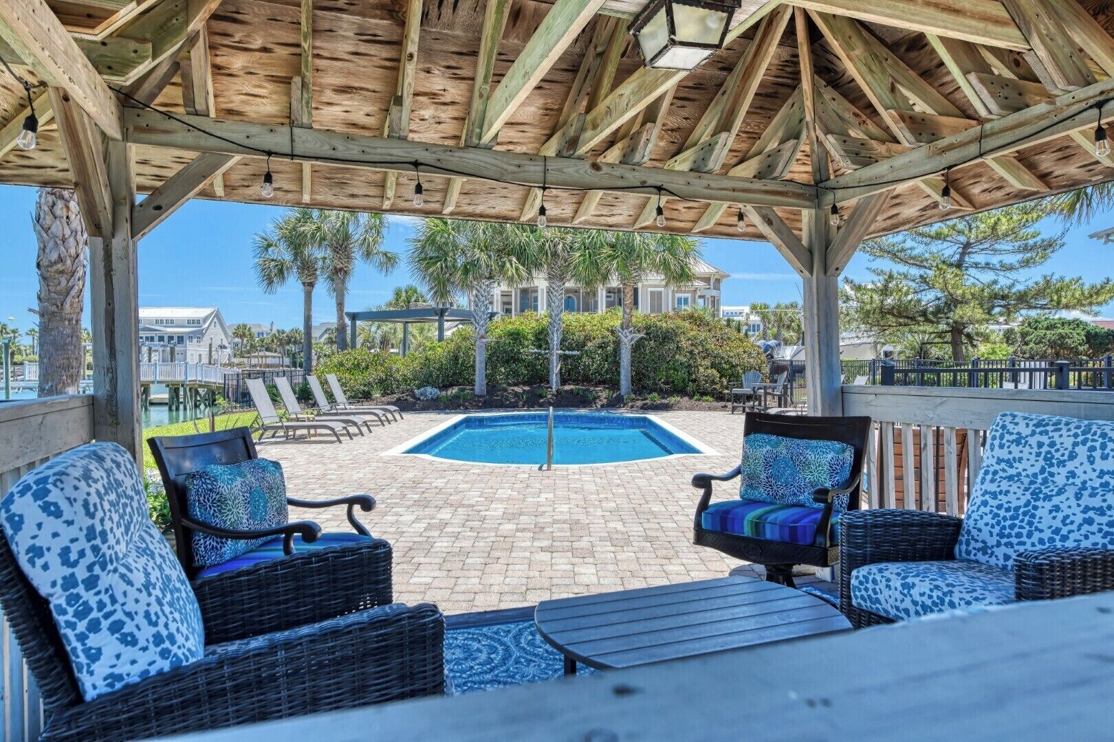 A covered outdoor area with a pool, wicker furniture, and a view of a building.