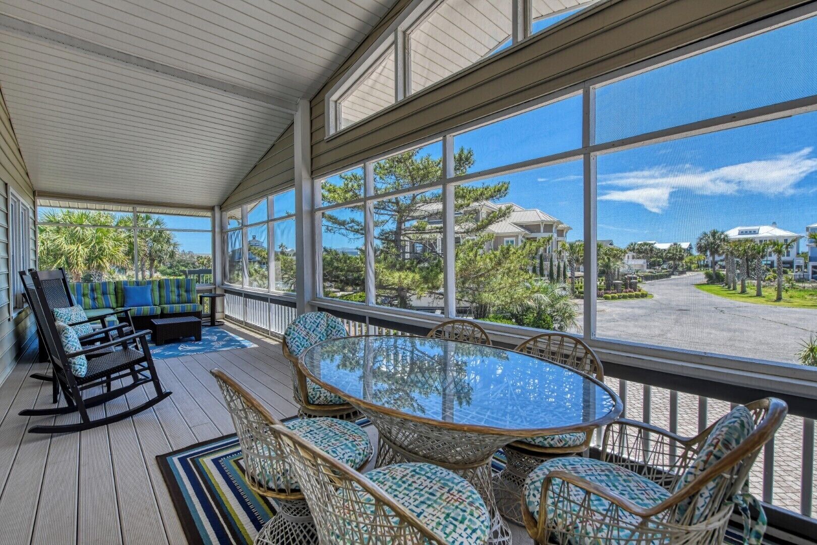A covered outdoor seating area with a glass table and wicker chairs, overlooking a residential neighborhood.