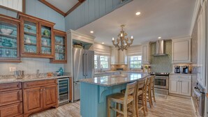 A kitchen with wooden cabinets, a central island with bar stools, a chandelier, and a large window. - Pop's Place in the private gated community of Inlet Harbour (Garden City Beach)