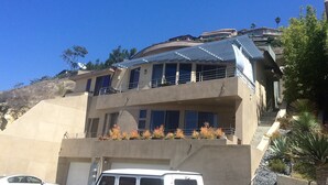 Ein mehrstöckiges Gebäude mit flachem Dach, großen Fenstern und einem Balkon mit Pflanzen.
