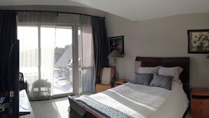 Ein Hotelzimmer mit Bett, Stuhl, Schreibtisch, Lampe und Blick ins Freie.