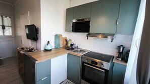 A compact kitchen with a microwave, stove, and oven, a small sink, and a window with curtains.