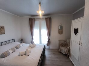 A bedroom with a bed, a bedside table, a wardrobe, a mirror, and a window with curtains.