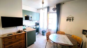 A compact kitchen with a microwave, stove, and sink. There's a dining table with chairs and a flat-screen TV mounted on the wall.