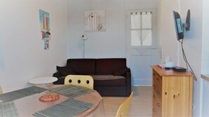 A small, cozy room with a dark brown sofa, a wooden cabinet, a small round table, and a TV mounted on the wall. - Résidence Les Althéas - Apartment 2 (Villers-sur-Mer)