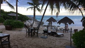 A beachside seating area with tables and chairs, thatched umbrellas, and lounge chairs. - Sleeps 5.  Rooftop infinity pool, 2 bed, 2.5 baths, 2nd floor. Walk to cafes. (Tulum)