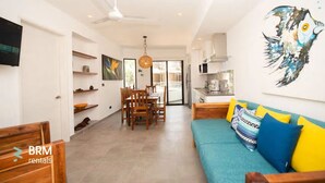 A modern living room with a sofa, a dining area, and a kitchen. - Sleeps 5.  Rooftop infinity pool, 2 bed, 2.5 baths, 2nd floor. Walk to cafes. (Tulum)