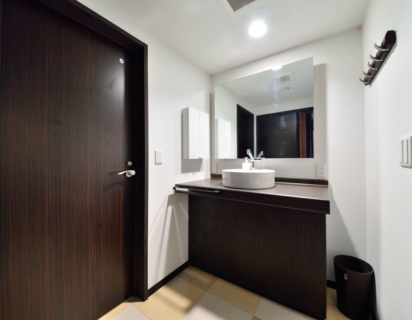 A modern bathroom with a dark wood door, white vanity, and a large mirror above the sink.