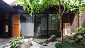 En traditionel japansk bygning med trædør, store glasruder og en stentøflset bed med et træ.
