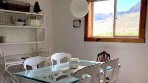 A dining area with a glass-top table, white chairs, and a window with a view of a mountainous landscape.