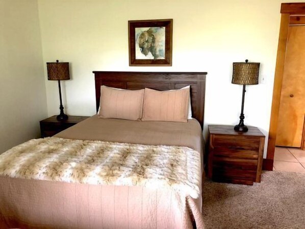 A neatly made bed with a fluffy blanket, two bedside lamps, and a framed picture on the wall.
