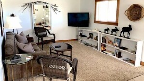 A living room with a sofa, chairs, a coffee table, a TV, and shelves with books and decorative items.