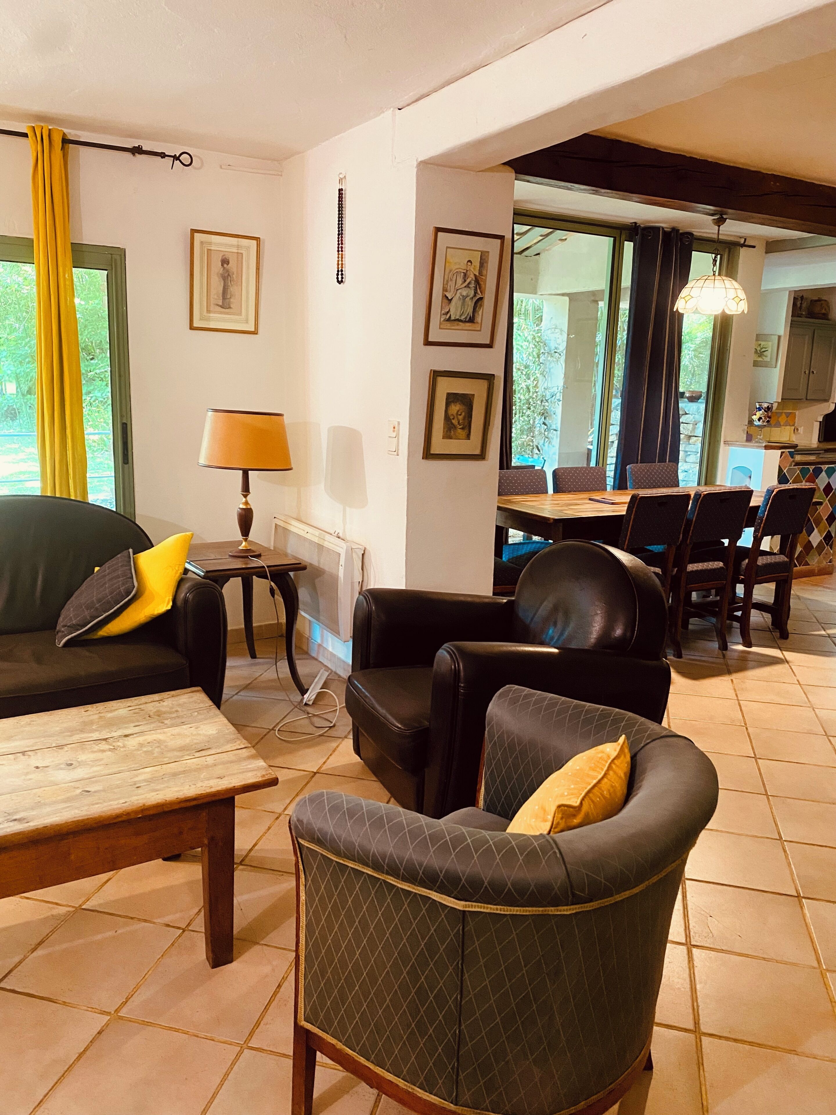 A living room with a sofa, armchair, and table, a dining area with chairs, and a kitchen in the background.