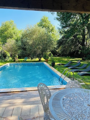 A swimming pool with a patio area, including a table and chairs, surrounded by trees.