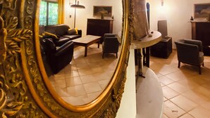 Uma sala de estar com um espelho grande e decorativo, um sofá, uma mesa de centro e um abajur.