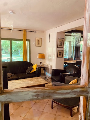 A living room with a sofa, armchair, and a coffee table. There is a window with a view of greenery outside.