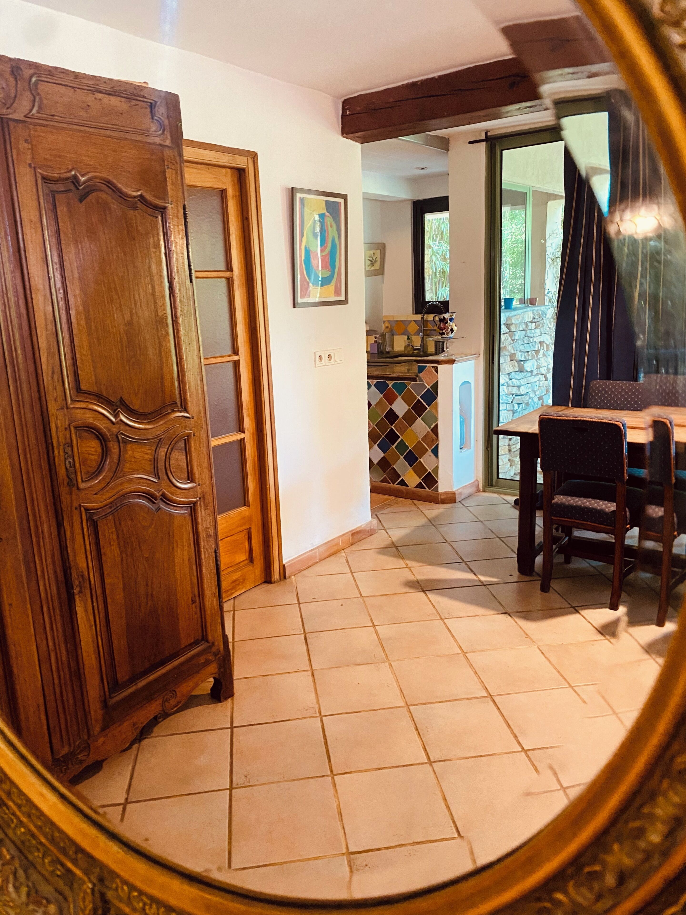 A dining area with a wooden table and chairs, a tiled floor, a wooden door, and a colorful backsplash.