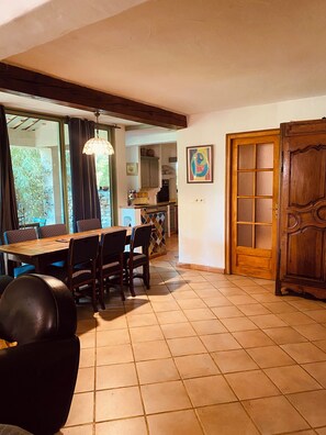 A dining area with a wooden table and chairs, a kitchen in the background, and a wooden door with glass panels.