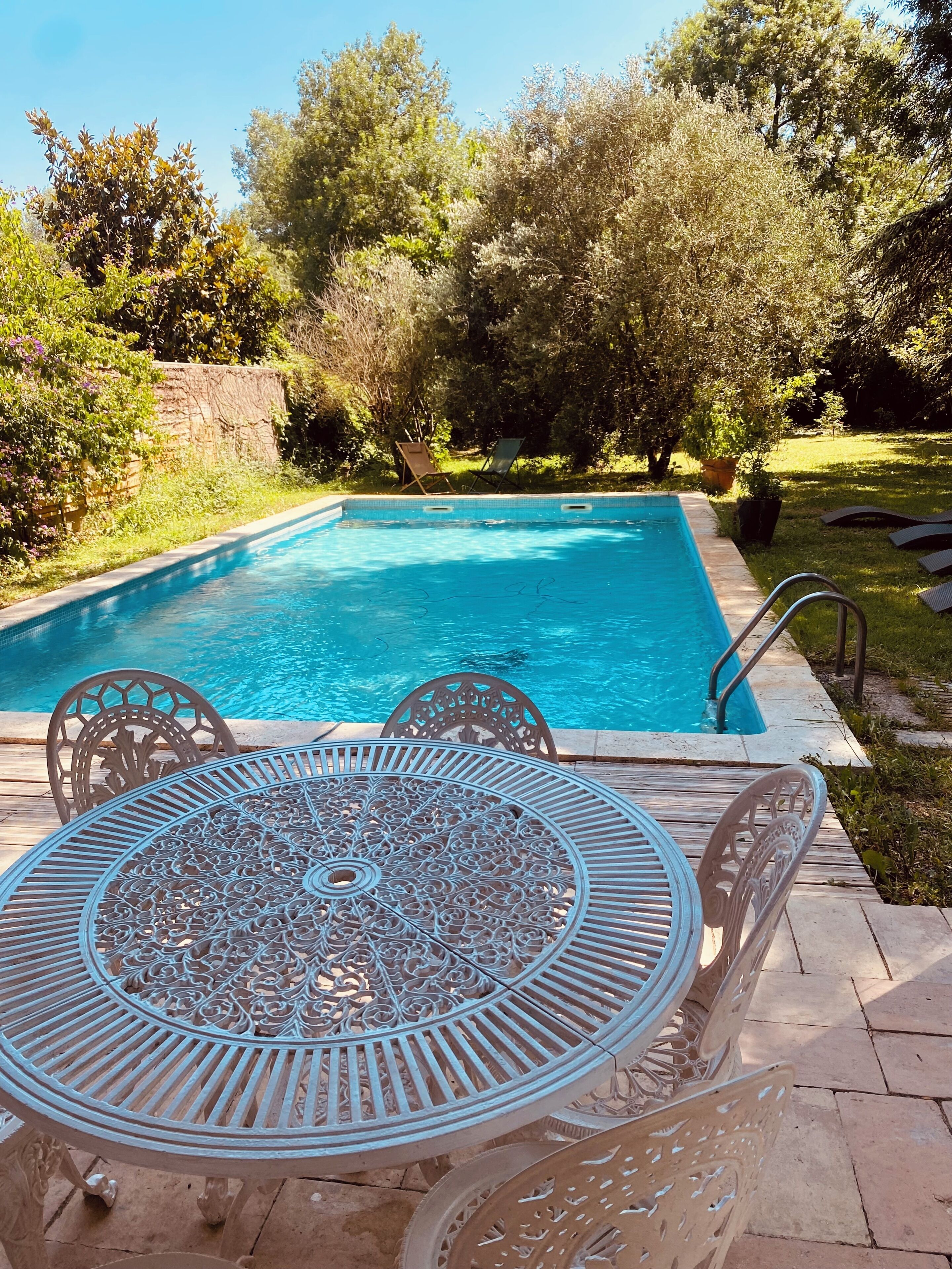 A rectangular swimming pool with a metal table and chairs in the foreground.