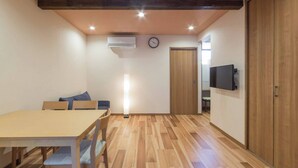 A room with a wooden table and chairs, a standing lamp, a clock, an air conditioner, and a wardrobe. - Japanese Modern Townhouse in Gion with Floor Heat (Kyoto)