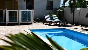 A swimming pool with two lounge chairs and a glass door.