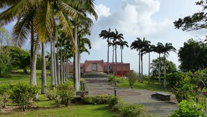 A building with a red facade, surrounded by a well-maintained lawn and palm trees.