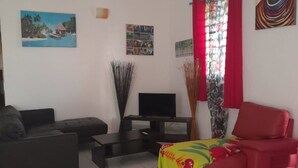 A living room with a sofa, a red armchair, a TV, and a painting of a tropical scene.