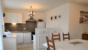 A modern kitchen with white cabinetry, a built-in oven, and a dining area with a table and chairs.