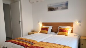 A double bed with white bedding and two decorative pillows, a wooden headboard, a small bedside table with a lamp, and a framed picture on the wall.