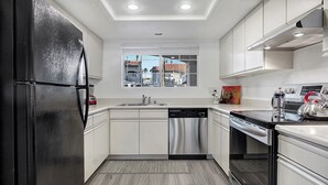 A modern kitchen with white cabinets, stainless steel appliances, and a window overlooking a cityscape.