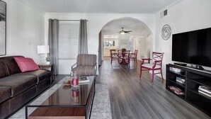 A modern living room with a sofa, coffee table, TV, and dining area.