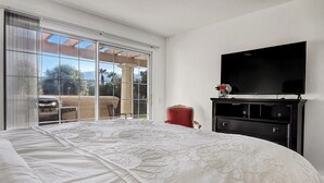 A bedroom with a large bed, a TV, and a sliding glass door leading to an outdoor patio.