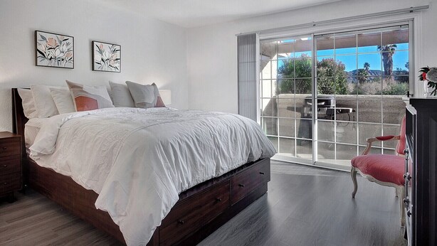 A bedroom with a large bed, a wooden dresser, a red chair, and a balcony with a view of the outdoors.