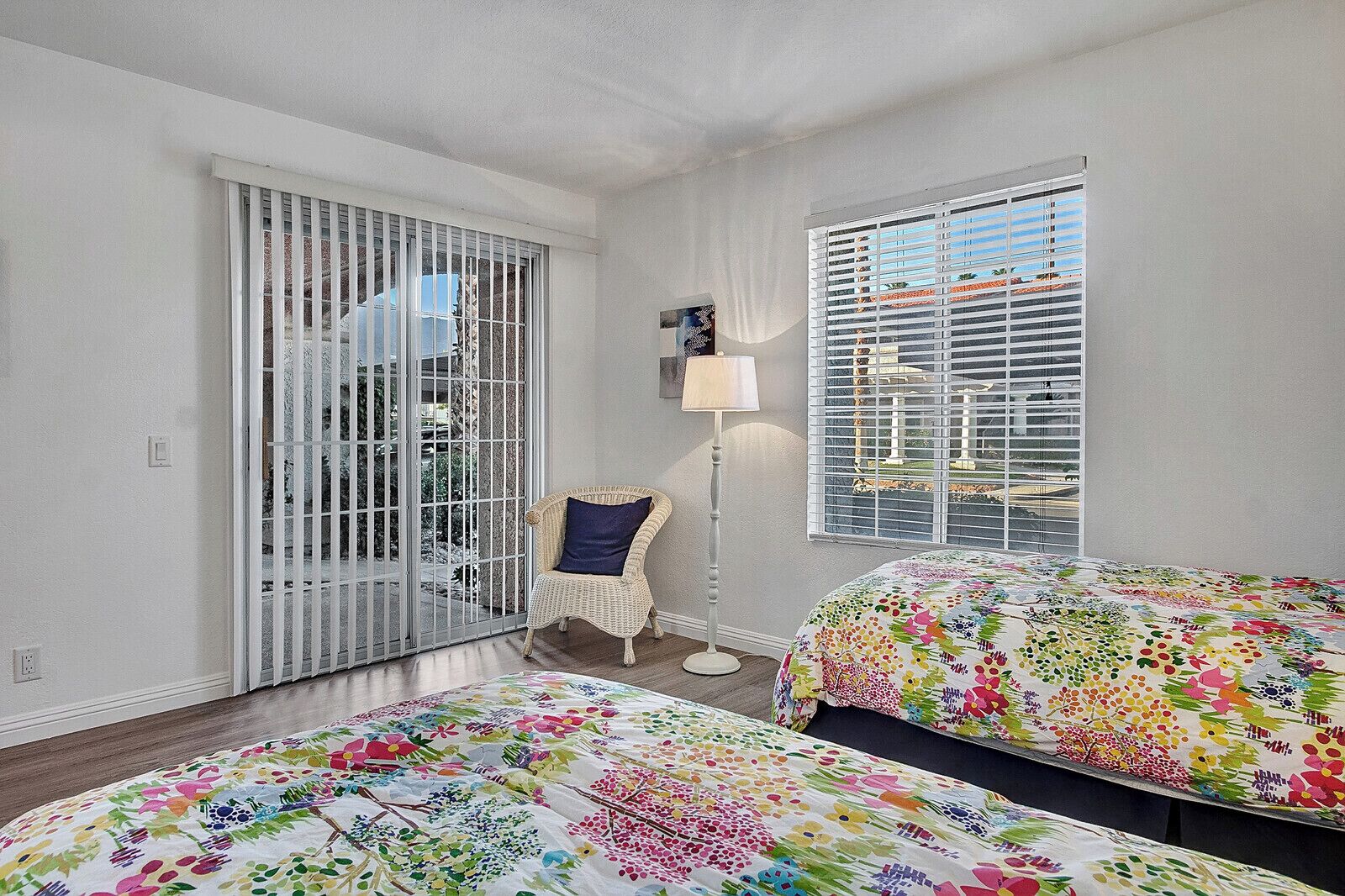 Ein Schlafzimmer mit zwei Betten, einem Sessel, einer Lampe und einem Fenster mit Jalousien.