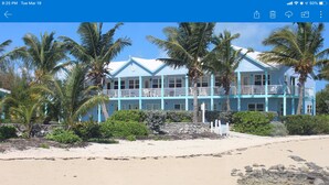 Een hotel aan het strand met meerdere balkons, palmbomen en een zandstrand.