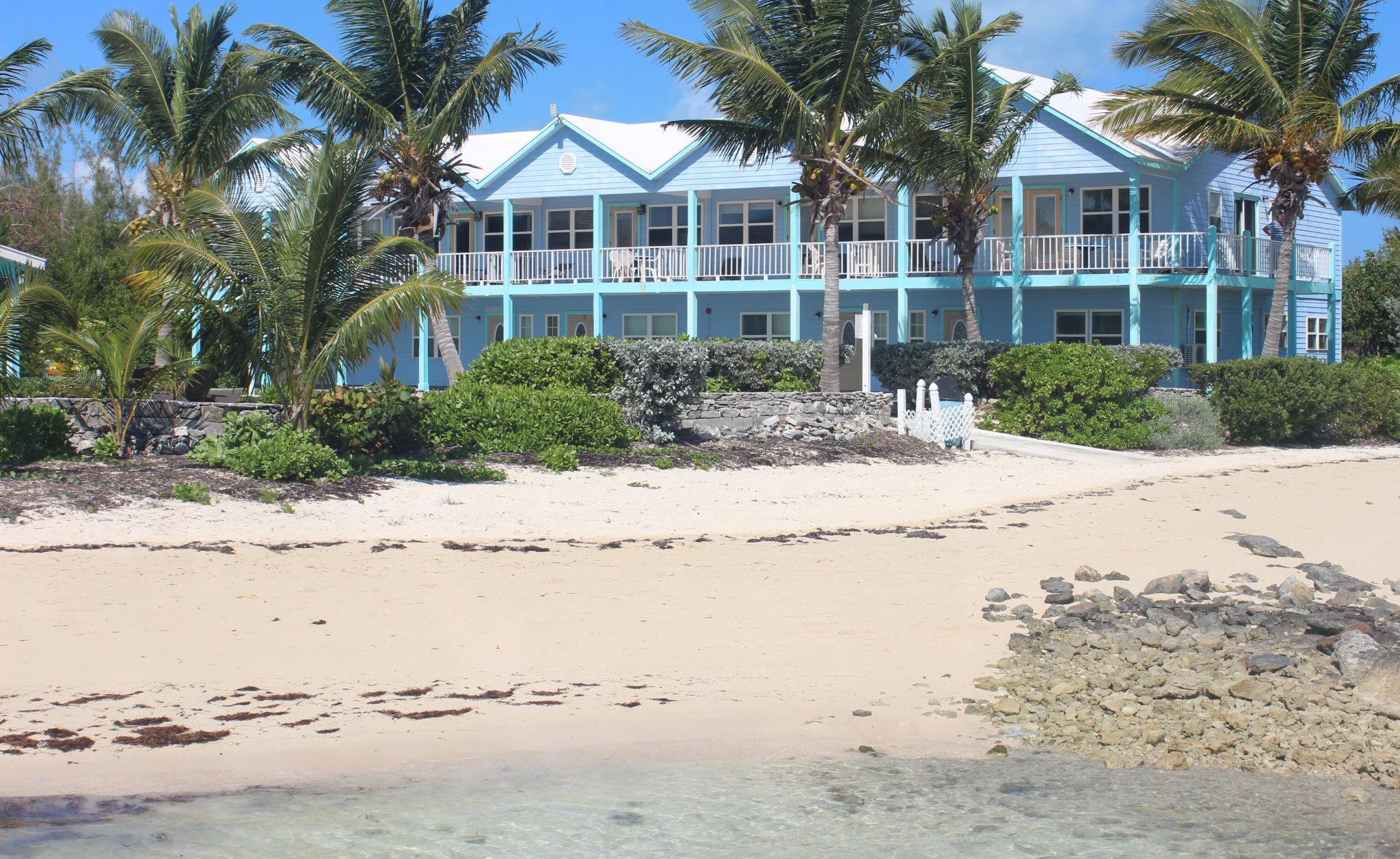 A beachfront hotel with multiple balconies, palm trees, and a sandy beach.