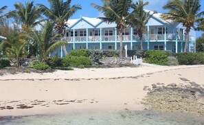 A beachfront hotel with multiple balconies, palm trees, and a sandy beach. - Newly renovated Oceanfront Townhouse with Stunning Views & Private Beach Access (George Town)