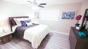 A bedroom with a bed, a nightstand, a dresser, a ceiling fan, and two paintings on the wall. - Gannet ·- Adorable Condo By Strip- Restaurants,Shopping (Las Vegas)