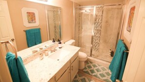A bathroom with a large mirror, a sink with toiletries, a toilet, and a shower with a glass door. - Gannet ·- Adorable Condo By Strip- Restaurants,Shopping (Las Vegas)