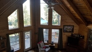 Una cabaña de madera con techos altos, ventanas grandes, ventilador de techo y chimenea.