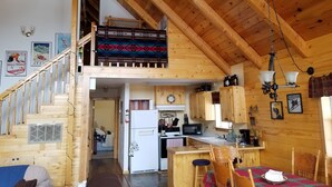 Interior de una cabaña de madera con habitación en el altillo, cocina y comedor.