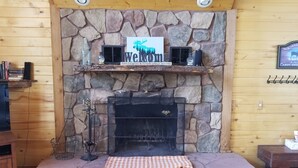 Una chimenea de piedra con un cartel de 'Welcome', un estante con libros y un cartel de 'Cabin Swede'.