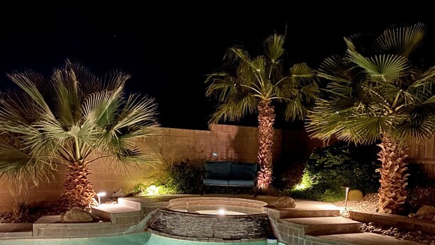 A nighttime swimming pool with palm trees and a stone wall. - Mountain & Sunset Views, Private Salt water Pool Spa, Putting Green, Spacious (Desert Hot Springs)