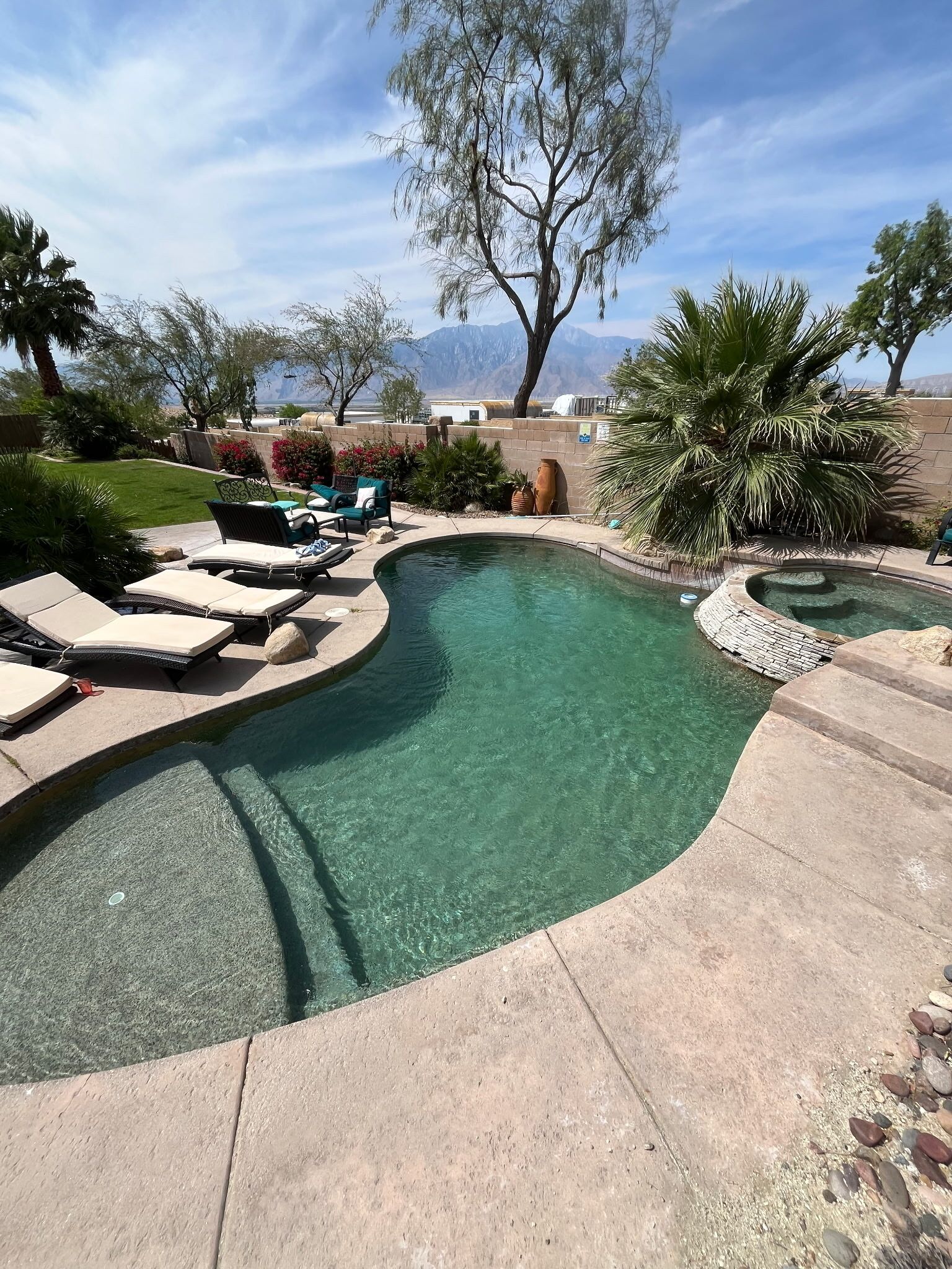 A clear swimming pool with lounge chairs and a view of mountains.