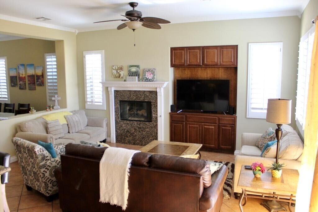 A living room with a fireplace, a ceiling fan, and a television.