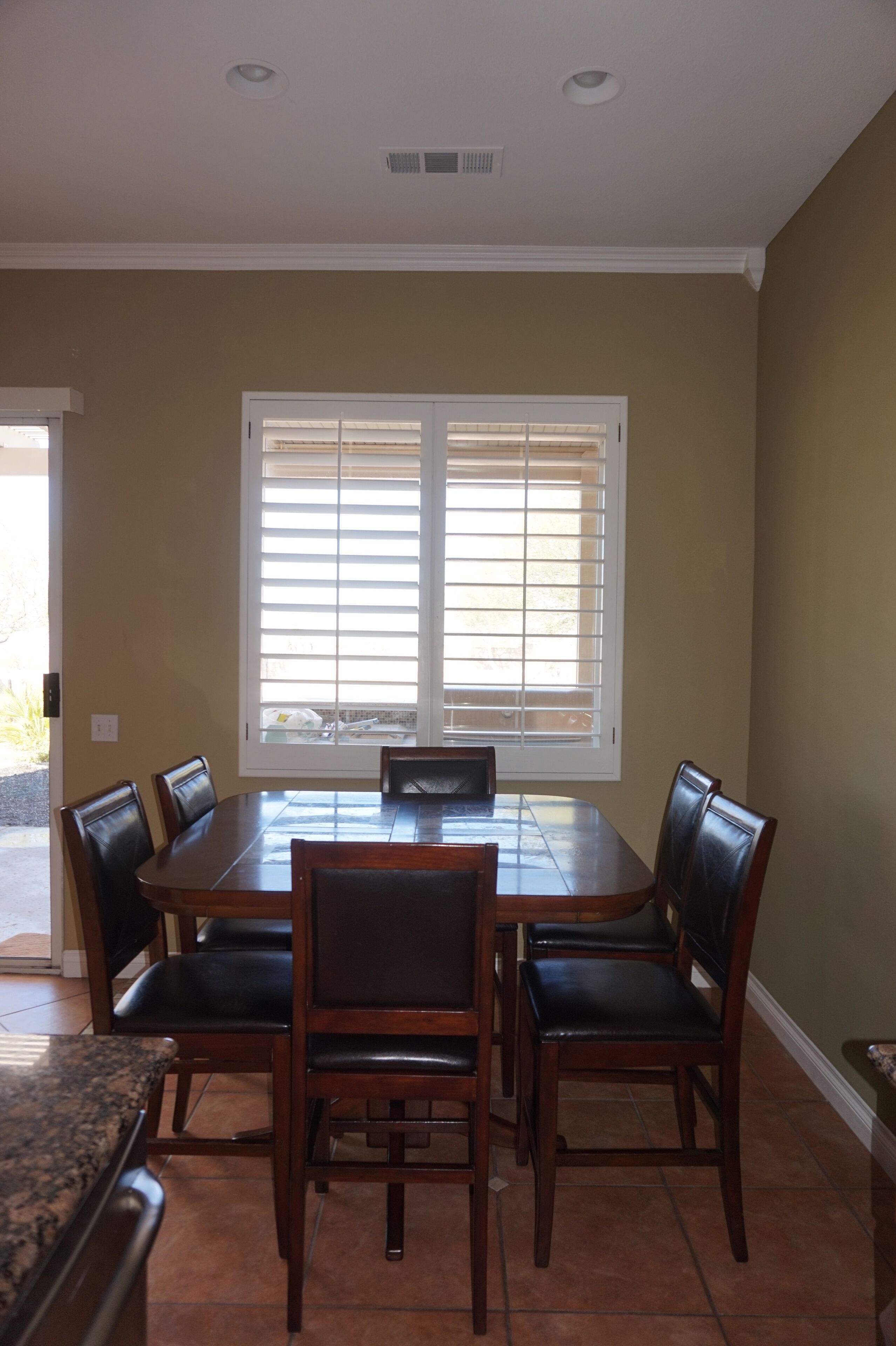 Un comedor con una gran mesa de madera y seis sillas, una ventana con persianas y un respiradero en el techo.