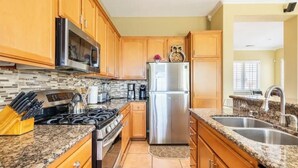 A kitchen with wooden cabinets, a stainless steel refrigerator, a stove, and granite countertops. - Mountain & Sunset Views, Private Salt water Pool Spa, Putting Green, Spacious (Desert Hot Springs)
