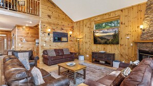 A log cabin interior with a living room featuring leather sofas, a coffee table, and a fireplace.